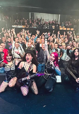 Photo souvenir du groupe Cobra Spell sur scène avec le public de l'A.R.C.A.D.E. en arrière-plan, illustrant l'ambiance intimiste et chaleureuse de la salle.